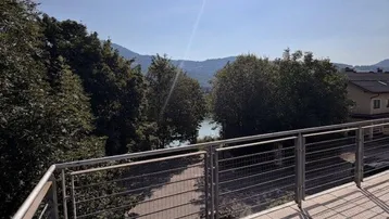 Große Sonnenterrasse mit Fliesenboden, Edelstahlgeländer und weitem Blick auf den See und die Berge.