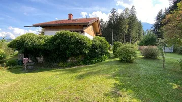 Idyllisches Haus mit großem Garten und Bergblick unter blauem Himmel an einem sonnigen Tag.