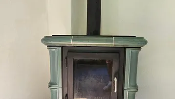 Detailansicht eines traditionellen Kachelofens mit grünen Fliesen und Holzfeuerung im Wohnbereich.