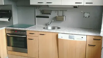 Funktionale Küche mit hellen Holzunterschränken, weißen Oberschränken und integrierten Geräten.
