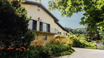 Traditionelles Haus mit Balkon und üppiger Bepflanzung, umgeben von grüner Natur und Bäumen.