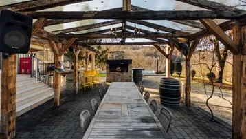 Rustikaler Essbereich im Freien unter einer Pergola mit großem Holztisch und Außenkamin.