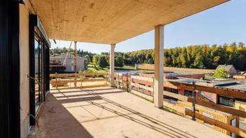 Geräumige, noch unfertige Terrasse mit Blick auf die umliegende Landschaft und Wald.