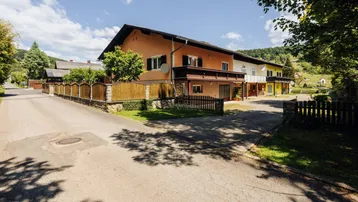 Ansicht des Mehrfamilienhauses von der Straße mit ländlicher Umgebung und sonnigem Wetter.