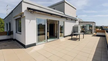 Moderne Gebäudefassade mit großer Dachterrasse, Schiebetüren und weitem Ausblick.