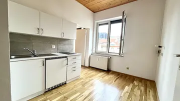 Funktionale Küchenzeile mit weißen Schränken, Spüle und einem Fenster, unter einer Holzbalkendecke.
