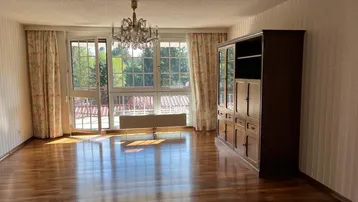 Helles Wohnzimmer mit Parkettboden, Kronleuchter und großen Fenstern mit Blick ins Grüne.