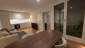 Moderner offener Wohn-Essbereich mit integrierter Küche, Holzboden und Zugang zu großen Fenstern.