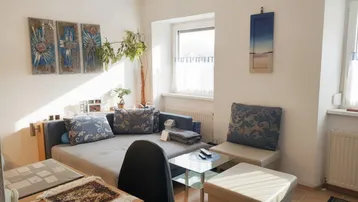 Helles Wohnzimmer mit Sofa, Schreibtisch und Blick nach draußen, durchflutet von natürlichem Licht.