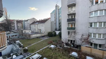 Blick von einem oberen Stockwerk auf einen begrünten Innenhof mit umliegenden Gebäuden und Balkonen.