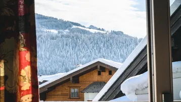 Blick aus dem Fenster auf schneebedeckte Berge und traditionelle Holzhäuser in winterlicher Landschaft.