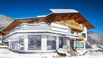 Winteransicht des Geschäftsgebäudes mit traditionellen Holzbalkonen und einer verschneiten Umgebung unter strahlend blauem Himmel.
