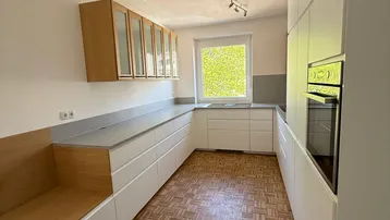 Moderne Küche mit weißen Schränken, Holzelementen, integrierter Sitzbank und Blick ins Grüne.