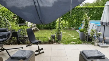 Große geflieste Terrasse mit Sonnenliege, Sonnensegel und Blick auf den Garten mit Pool.