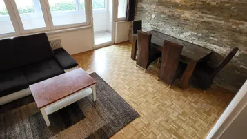 Geräumiger Wohn-Essbereich mit Parkettboden, moderner Steinwand und Zugang zum Balkon.