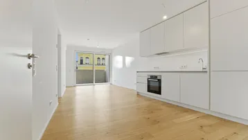 Heller Wohn- und Essbereich mit integrierter Küche, Parkettboden und Zugang zum Balkon.