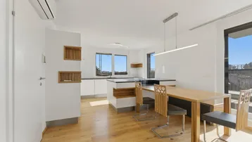 Heller offener Wohn- und Essbereich mit moderner Küche, Holzboden und Zugang zum Balkon.
