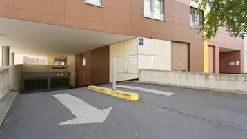 Einfahrt zu einer Tiefgarage unter einem modernen Wohngebäude mit brauner Fassade und Pfeilmarkierungen.