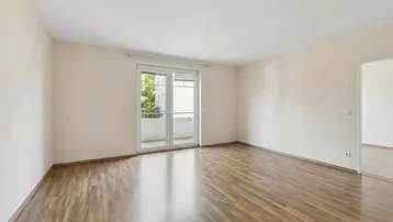Helles, leeres Wohnzimmer mit Holzboden und Zugang zu einem Balkon.