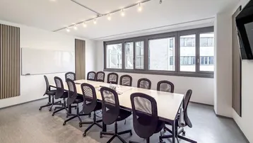 Moderner Konferenzraum mit großem Tisch, ergonomischen Stühlen und natürlichem Lichteinfall durch breite Fenster.