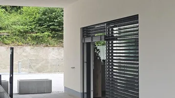 Überdachter Außenbereich mit Zugang zum Gebäude und Blick auf die grüne Umgebung.