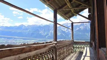 Traditioneller Holzbalkon mit geschnitztem Geländer und weitem Blick auf die Berge und das Tal.