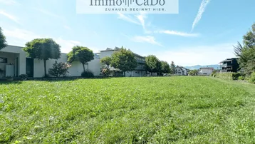 Weitläufige Grünfläche vor modernen Wohngebäuden mit Bergblick unter blauem Himmel.