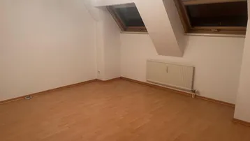 Heller Raum im Dachgeschoss mit schrägen Wänden, Laminatboden und Dachfenstern.