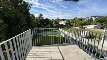 Geräumiger Balkon mit Fliesenboden und Blick auf eine grüne Wiese und Bäume.