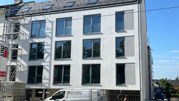 Neubau-Mehrfamilienhaus mit moderner Fassade und großen Fenstern, umgeben von Baugerüsten.