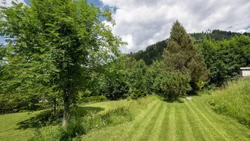 Gepflegter Rasenbereich mit Bäumen und Blick auf die bewaldeten Hügel unter einem bewölkten Himmel.