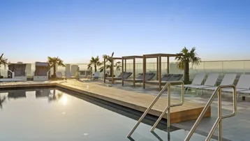 Dachterrasse mit Infinity-Pool, Liegestühlen und Panoramablick über die Stadt bei Sonnenuntergang.