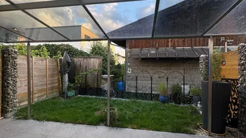 Überdachte Terrasse mit modernen grauen Fliesen und angrenzendem kleinen, eingezäunten Gartenbereich.