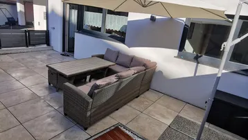Große gepflasterte Terrasse mit bequemen Outdoor-Möbeln und Sonnenschirm, ideal zum Entspannen im Freien.