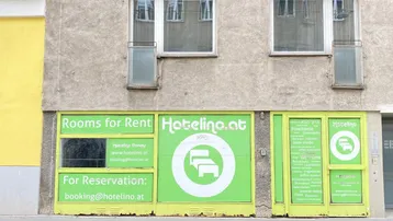 Fassade eines älteren Gebäudes mit großen grünen Werbeschildern für Zimmervermietung und Fenstern im Obergeschoss.