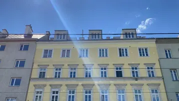 Gelbe Altbaufassade mit vielen Fenstern unter blauem Himmel und Sonnenschein.