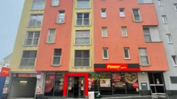 Mehrstöckiges Gebäude mit gelber und oranger Fassade und einem Penny-Markt im Erdgeschoss.