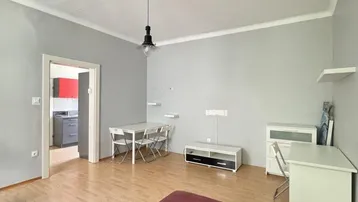 Geräumiges Wohnzimmer mit Parkettboden, rotem Sofa und Blick in die Küche.