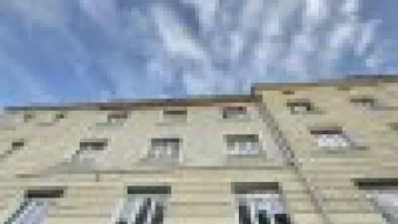 Fassade eines Mehrfamilienhauses mit zahlreichen Fenstern unter einem bewölkten Himmel.