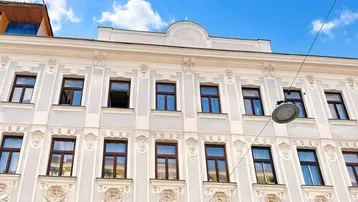 Fassade eines Altbaus mit vielen Fenstern und dekorativen Elementen unter strahlend blauem Himmel.