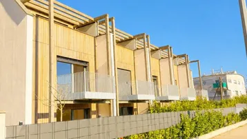Reihe moderner Stadthäuser mit Holzfassaden, Balkonen und gepflegten Hecken entlang der Straße.