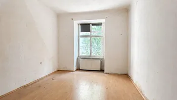 Leeres Zimmer mit Holzboden und Fenster, bereit für eine Renovierung.