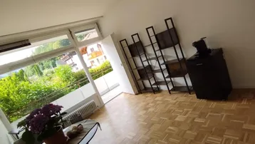 Helles Wohnzimmer mit Parkettboden, großen Fenstern und Blick ins Grüne.