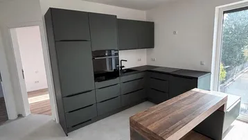 Moderne Küche mit dunklen Schränken, Holzelementen und Zugang zur Terrasse.