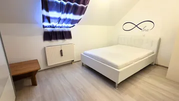Helles Schlafzimmer im Dachgeschoss mit weißem Bett, schrägen Wänden und Holzboden.