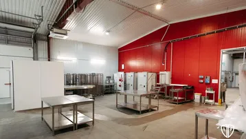Große Industriehalle mit roter Akzentwand, Edelstahltischen und hohen Decken, geeignet für Produktion oder Lager.
