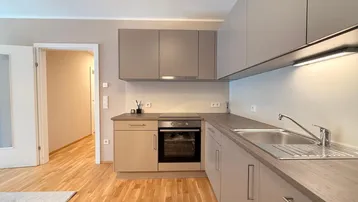 Moderne Küche mit beigefarbenen Schränken, Holzarbeitsplatte und Parkettboden.