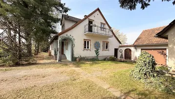 Ansicht des Hauses mit kleinem Balkon, Vorgarten und Zufahrt unter Bäumen.