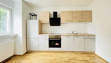 Moderne Einbauküche mit hellen Holzschränken, Kochfeld, Backofen und Dunstabzugshaube.