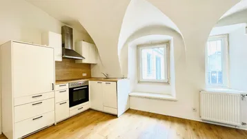 Helle Küche mit weißen Schränken, Holzarbeitsplatte, gewölbter Decke und Fenster mit Heizkörper.